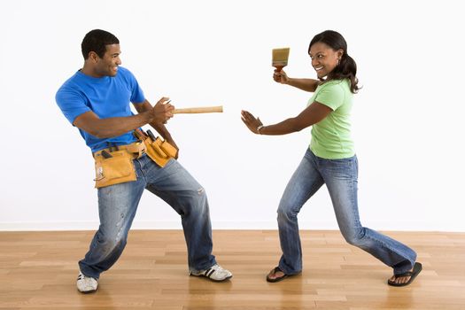 African American man and woman play fighting with household tools.