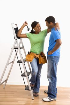 Portrait of smiling African American male and female couple with home repair tools and ladder.