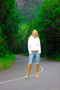 Blond girl standing right in the middle of the mountain road