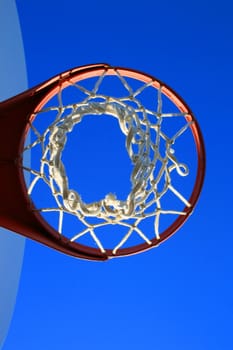 Basketball net and backboard over clear blue sky.
