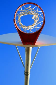 Basketball net and backboard over clear blue sky.
