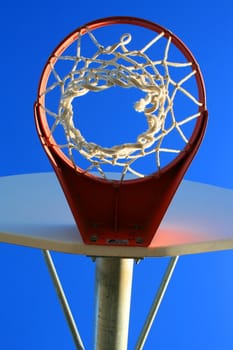 Basketball net and backboard over clear blue sky.
