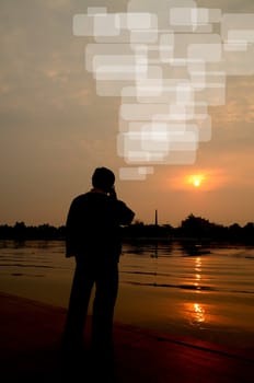 Silhouette image of business man made a phone call beside the river at sunset