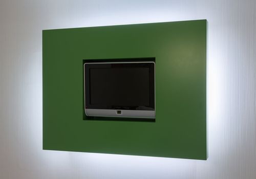Modern TV screen set in green surround against white wall of hotel room