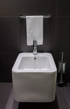 Details of modern square bidet in black tiled bathroom