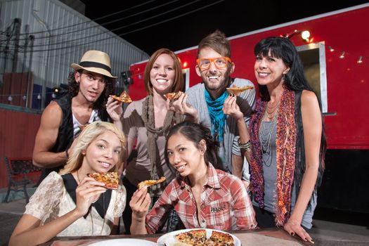 Six smiling mixed people holding pizza slices in front of food truck