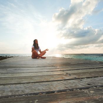 Young beautiful woman in lotus pose meditating near sea alone