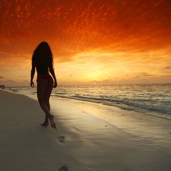 Young woman walking on beach under sunset light