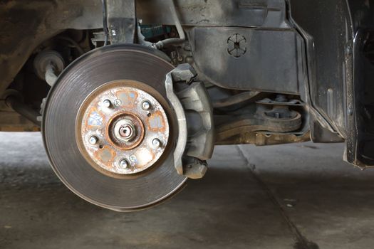 Front disk brake on car in process of damaged tyre replacement. The rim is removed showing the front rotor and caliper.