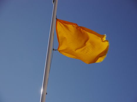 Yellow flag waving in the breeze against a blue sky.