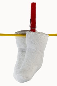 two white baby sox on yellow clothesline with clothespin in white background