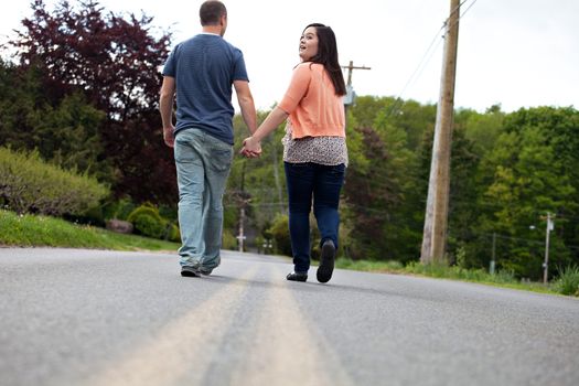 Young happy couple enjoying each others company outdoors walking down an empty road with the woman looking back at the viewer. Plenty of copy space.