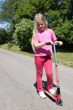 little girl rides a scooter on a rural road