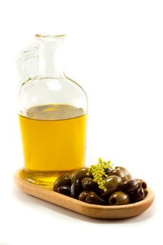 A glass bottle full of olive oil on a wooden plate with mixed olives