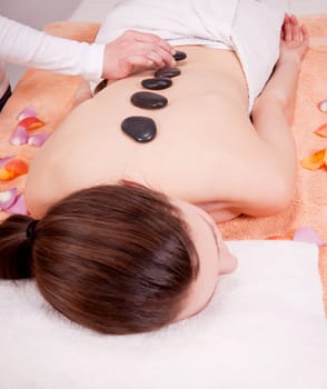 young attractive woman get hot stone massage by professional in wellness spa salon