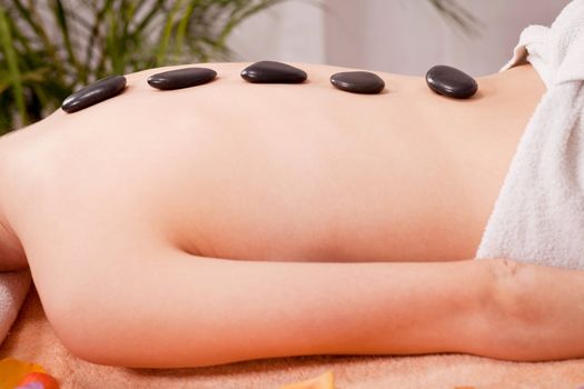 young attractive woman get hot stone massage by professional in wellness spa salon