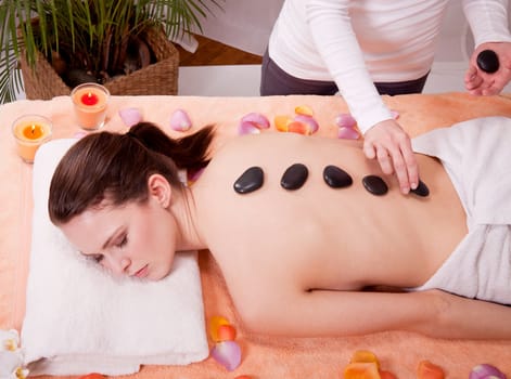 young attractive woman get hot stone massage by professional in wellness spa salon