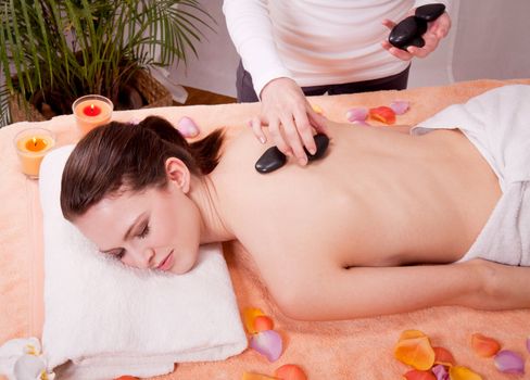 young attractive woman get hot stone massage by professional in wellness spa salon