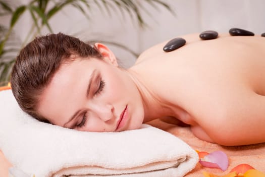 young attractive woman get hot stone massage by professional in wellness spa salon