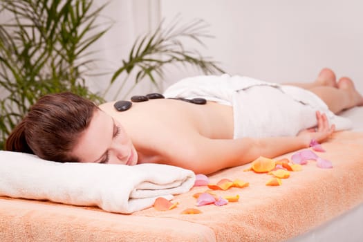 young attractive woman get hot stone massage by professional in wellness spa salon