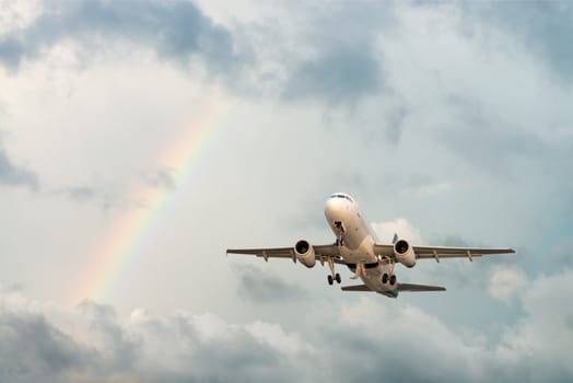 Airplane flying in cloudy sky with rainbow after rain