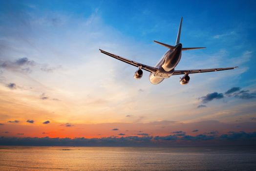 Airplane flying above tropical sea at sunset 