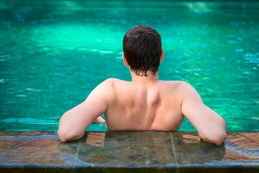 Back view of young men relaxing in a swimming pool on a poolside in tropical resort