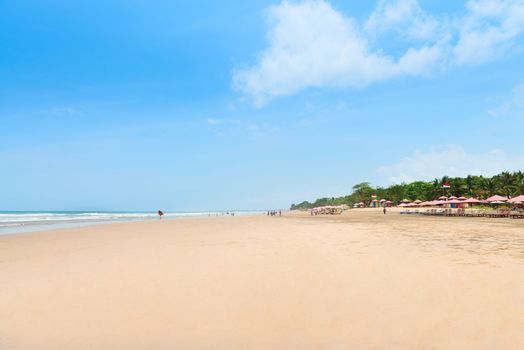 Wide sand beach with tourists, umbrellas and beds. The five km long sandy stretch of Kuta, Bali, Indonesia.