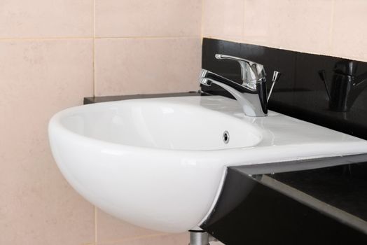 Modern ceramic hand wash basin with chrome water mixer tap in hotel washroom interior 
