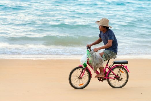 PHUKET, THAILAND - FEB 15: Old native local man bicycling along a sand beach on Feb 28, 2013 in Phuket, Thailand. Small law bicycles are common among Thailanders 