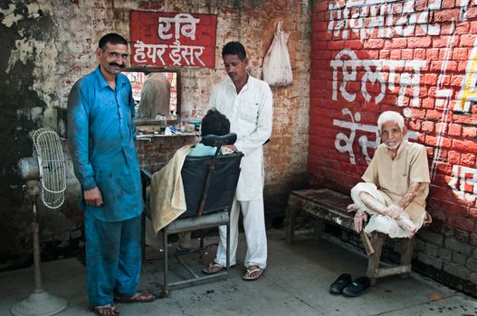 AMRITSAR, INDIA - AUG 28: Barber shaving a man in the street mobile barber's and two men wait on Aug 28, 2011 in Amritsar, India. It is very common barber's type in India.