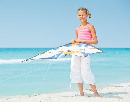 Young cute girl playing with a colorful kite on the tropical beach.