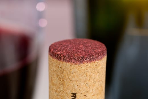 Cork from red wine bottle in front of glass of wine and green bottle out of focus