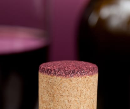 Cork from red wine bottle in front of glass of wine and green bottle out of focus
