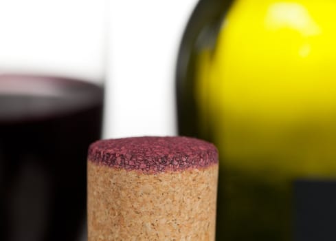 Cork from red wine bottle in front of glass of wine and green bottle out of focus