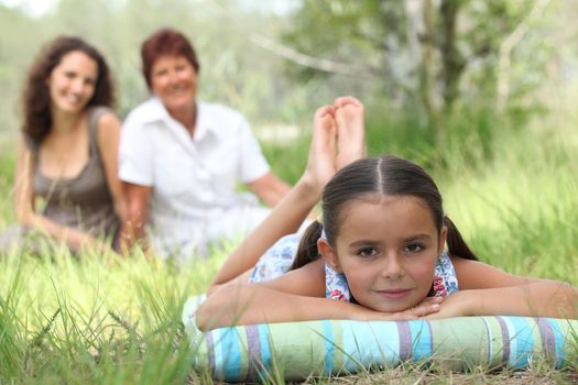 little girl relaxing in park with mother and grandma in background