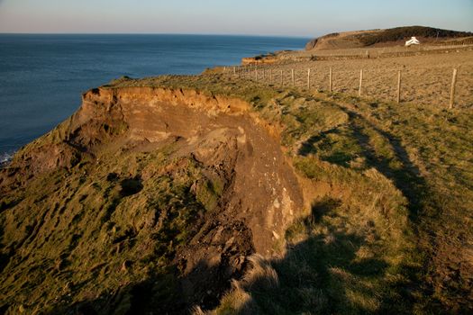 A footpath on a grass  passes an area of landslide above the sea.
