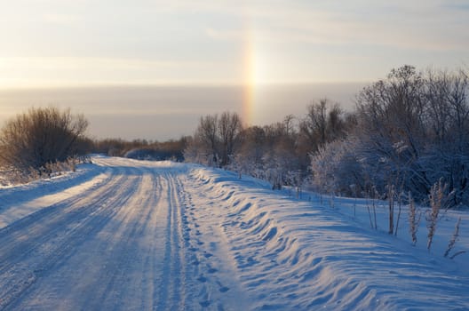 Road in a countryside in sunny winter rainbow day.Frozen trees in snowy field
