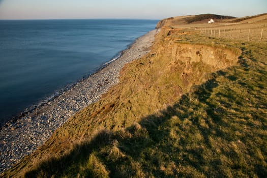 The Wales coast path follows grassy fields above the pebble beach of West Shore, Trefor, Lleyn Peninsular, Wales, UK.