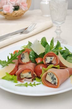 Appetizer of rolls with ham and blue cheese in a salad of lettuce with slices of Parmesan cheese