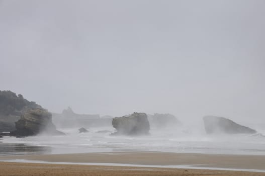 Rocks and beach under the rain into the mist during a sadly day