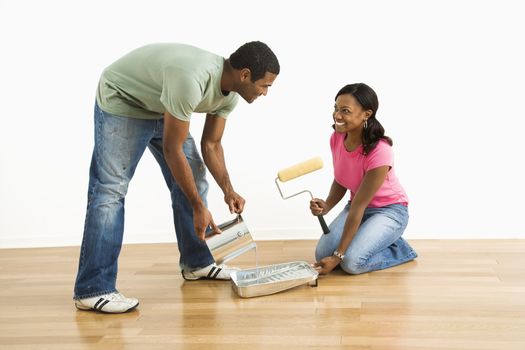 Smiling African American man pouring paint into tray as female looks on.