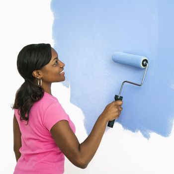 African American woman painting wall blue.