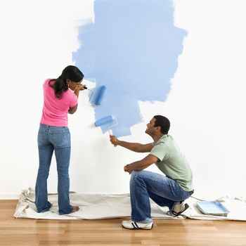 Smiling African American male and female couple painting wall blue.