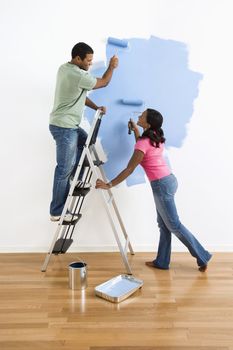 African American male and female couple painting wall blue and smiling at each other.