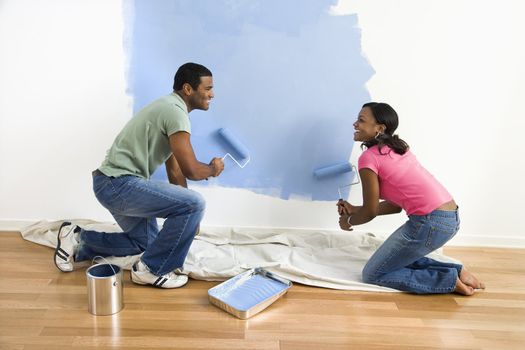 African American male and female couple painting wall blue.