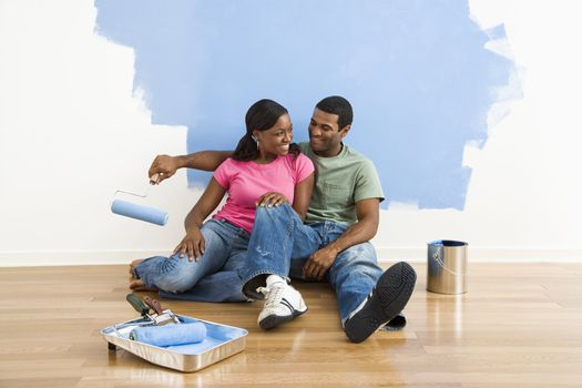 African American couple relaxing together next to half-painted wall and painting supplies.