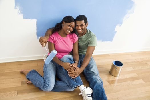 African American couple relaxing together next to half-painted wall and painting supplies.