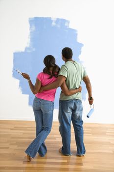 African American couple standing together looking at half-painted wall.