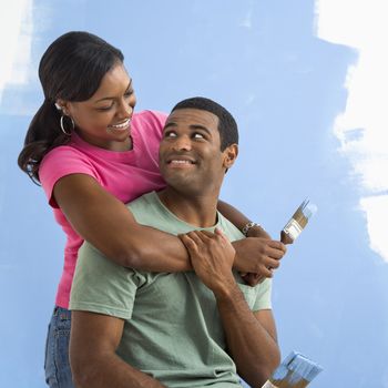 Portrait of African American male and female couple next to half-painted wall.